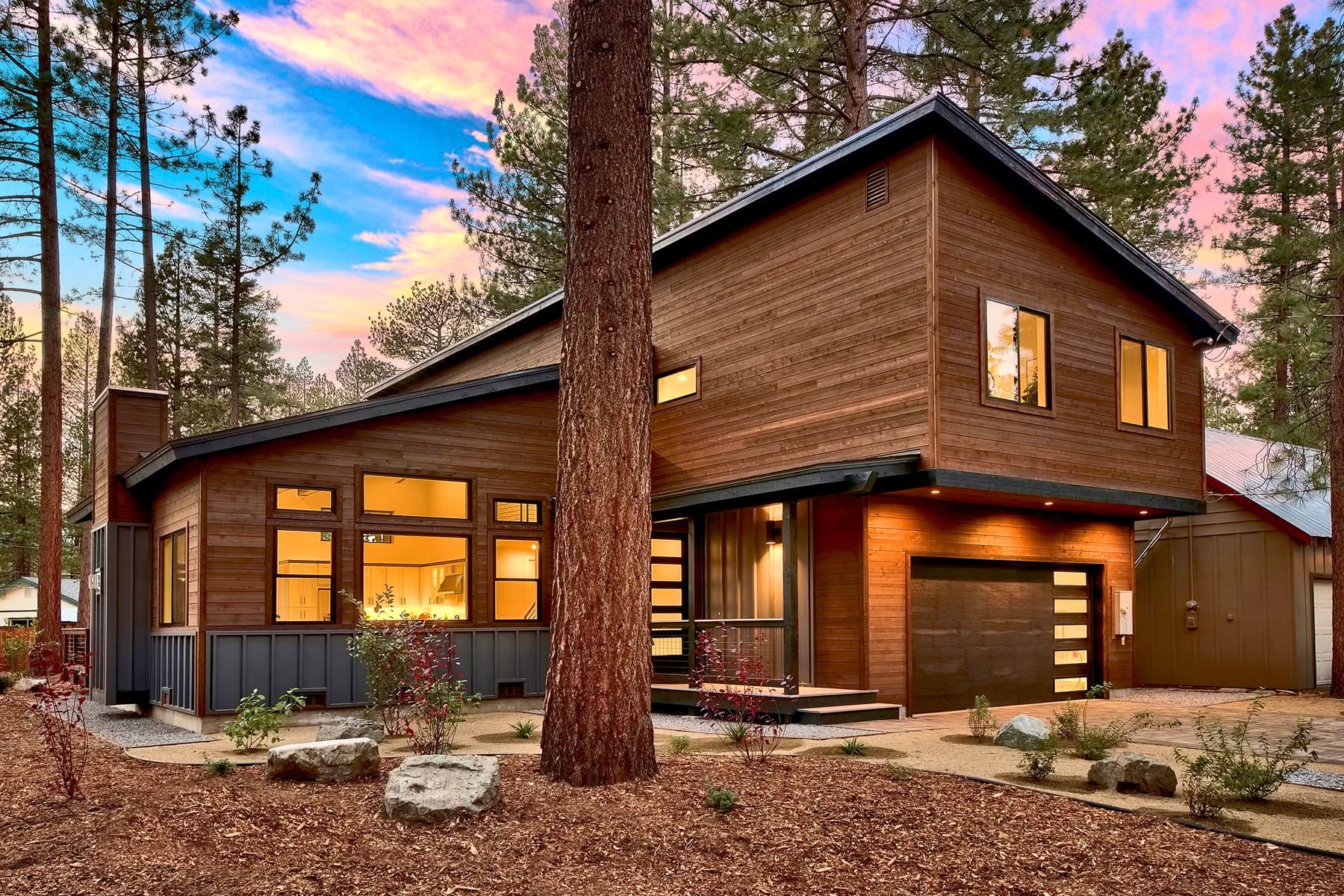 Cedar-sided custom home at twilight with a sunset sky over the pines and a landscaped front yard.